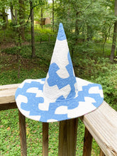 Load image into Gallery viewer, A blue and white patterned wide-brim witch's hat resting on a wooden deck railing with a forest background.